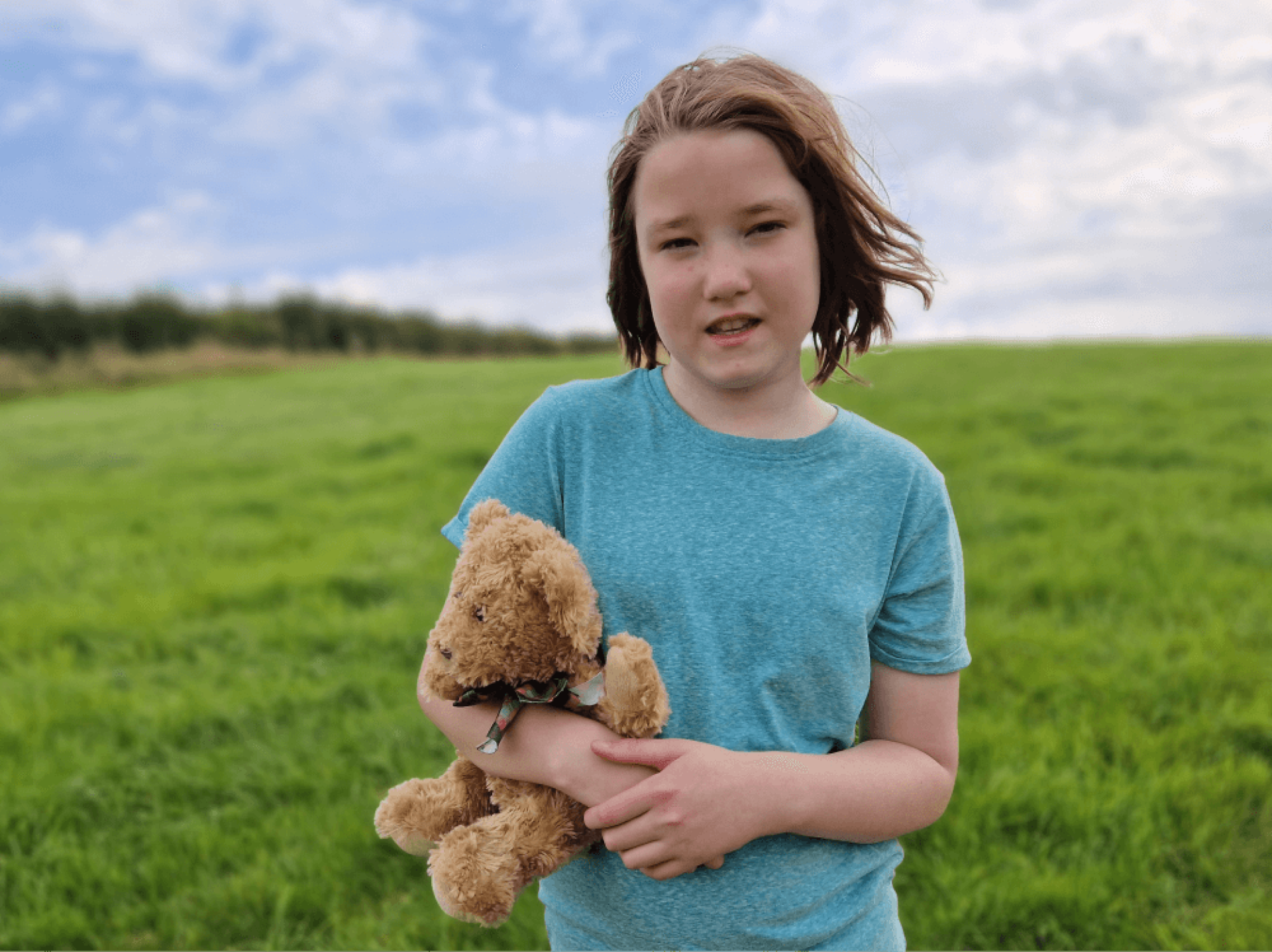 a child holding a teddy bear in a field